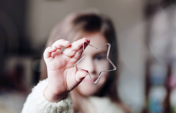 Cute little girl holding big christmas star and looking through it. - Foto, Bild