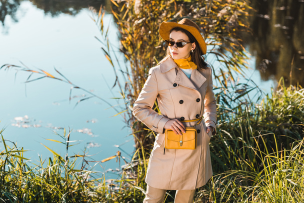 elegant stylish woman in trench coat and hat posing with yellow bag outdoors  - Photo, Image