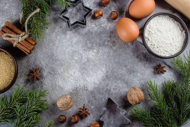 Weihnachtsbäckerei-Konzept. Zutaten zum Kochen von Weihnachtsgebäck - Mehl, brauner Zucker, Eier, Gewürze und Weihnachtsdekoration auf grauem Steingrund. Ansicht von oben mit Kopierraum. - Foto, Bild