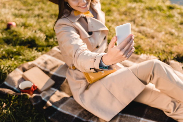 vista parcial de la mujer con estilo en sombrero tomando selfie en el teléfono inteligente al aire libre
  - Foto, imagen