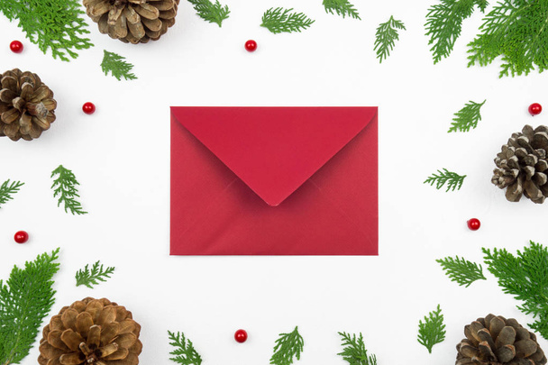 Creative Christmas layout. Red envelope, twigs and pinecones on white background whit copy space. Border arrangement. Flat lay top view.  - Fotó, kép