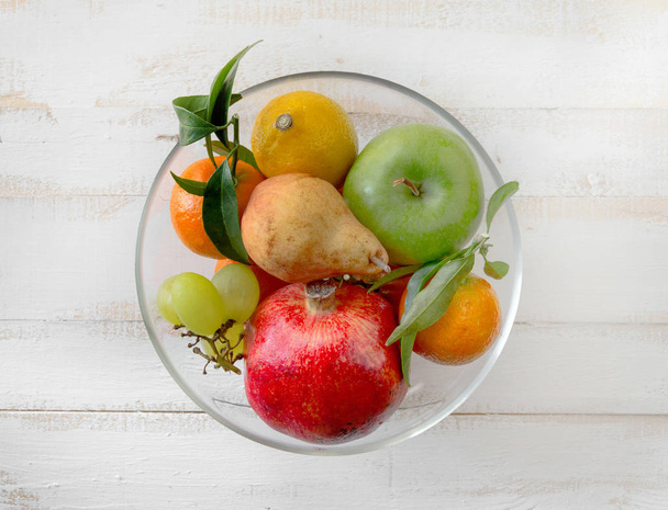 glass bowl with fresh fruits on white wooden table - Valokuva, kuva