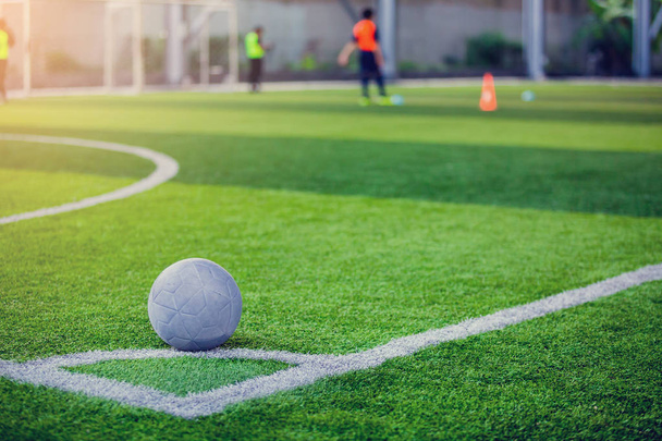 Μπάλα στην τεχνητή τύρφη στην γωνία του γηπέδου ποδοσφαίρου με φόντο θολή παίκτη. - Φωτογραφία, εικόνα