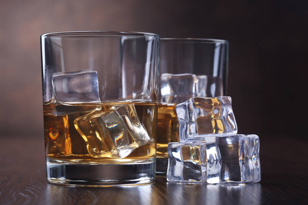 Gläser mit Whiskey und Eiswürfeln auf braunem Hintergrund - Foto, Bild