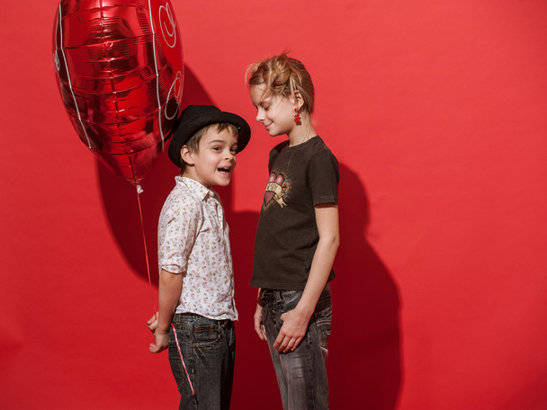 Girl and boy with big hearty red balloon on the red background. - Foto, imagen