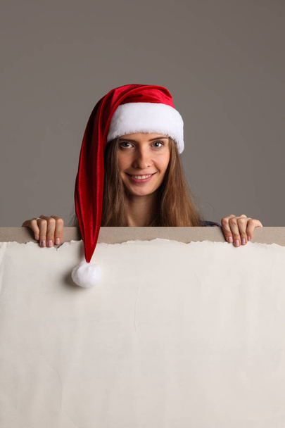 Santa girl holding blank vintage sign billboard. Christmas woman in Santa hat showing paper sign. - Foto, immagini