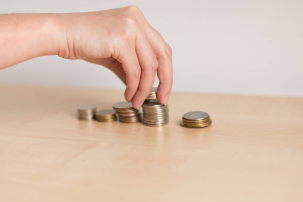 Hand is putting money coin on coin stacks divided by type of coin on wooden table in soft focus, business and financial concept. - Fotografie, Obrázek