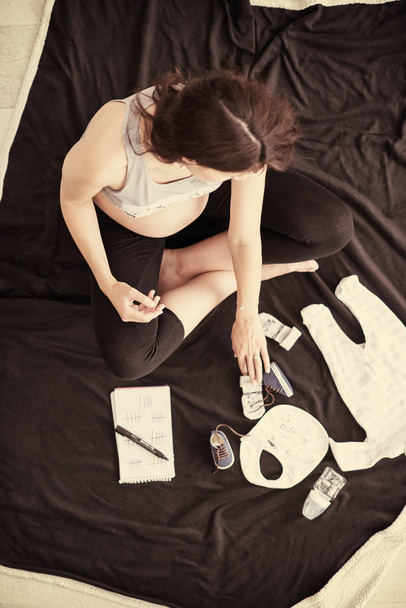 a pregnant woman at home on the floor checking list of baby clothes preparing for going to maternity hospital top view.Pregnancy, birth concept - Фото, зображення
