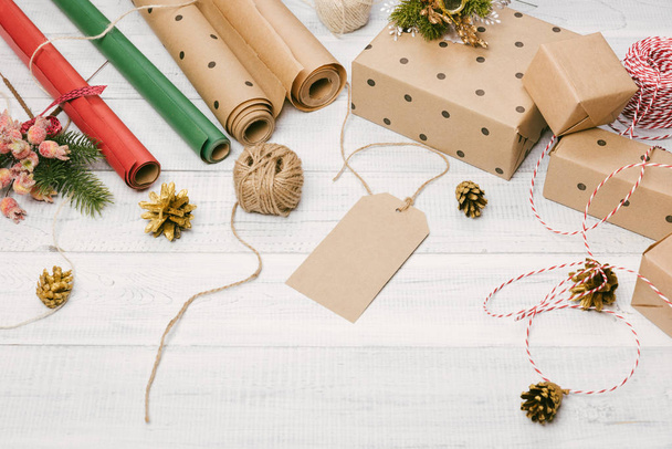Christmas presents and gift boxes wrapped in kraft paper on a wooden table, fir-tree branches and decoration, top view. Flat lay, copy space for text. - Фото, изображение
