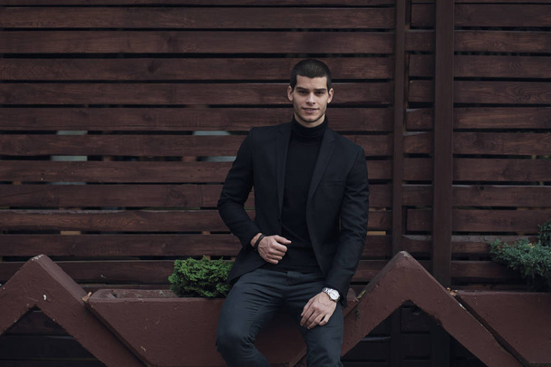 Retrato de jovem confiante, homem elegante, vestindo um terno, sentado contra a parede de madeira
. - Foto, Imagem