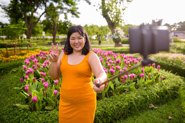 Femme asiatique prenant selfie avec téléphone mobile attacher à selfie bâton dans le parc
 - Photo, image