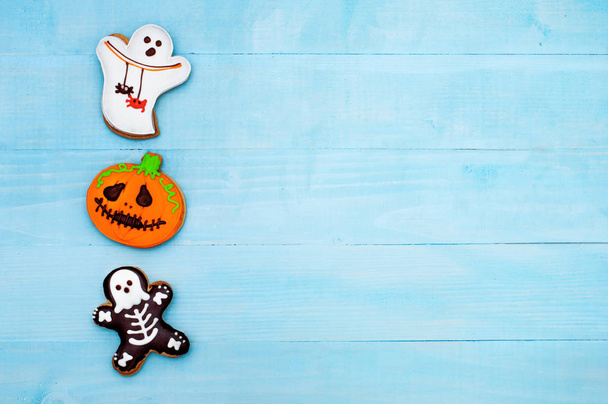 Halloween-Lebkuchengespenst, Skelett und Kürbis auf blauem Holzgrund. Gruselige Süßigkeiten auf dem Tisch. Kopierraum. Flatlay - Foto, Bild