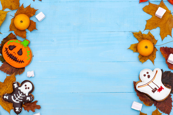 Halloween-Lebkuchengespenst, Skelett und Kürbis auf blauem Holzgrund. Gruselige Süßigkeiten mit Herbstblättern und Kerzen auf dem Tisch. Kopierraum. Flatlay - Foto, Bild