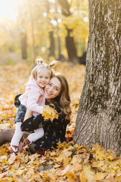 Young mother with beautiful daughter are walking in the park in the golden autumn. Have fun, laugh, take a selfie. - Photo, Image