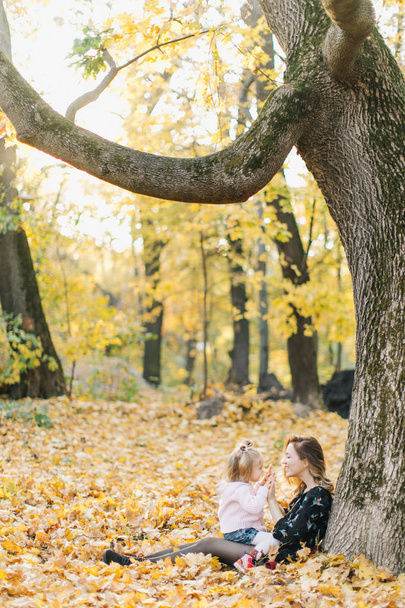 Young mother with beautiful daughter are walking in the park in the golden autumn. Have fun, laugh, take a selfie. - Фото, зображення