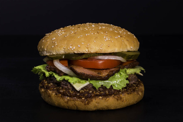 Burger with beef, marinated cucumber, onion, salad, tomatoes and bacon - Фото, зображення