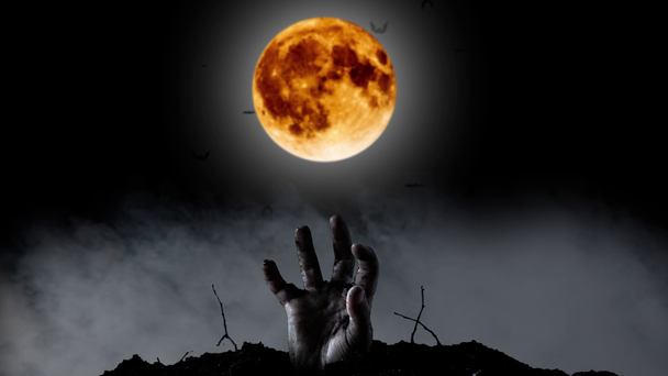 Menselijke hand klimt in de begraafplaats achter een heldere gele maan en een blauwe schittert. Zwarte rokerige achtergrond - Video