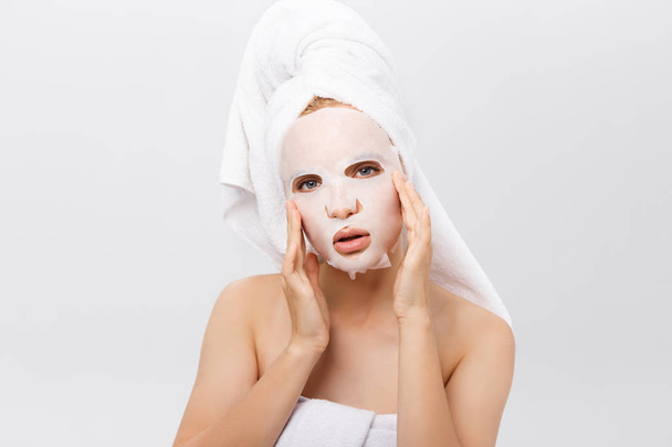 Beauty Skin Care Concept - Mulher branca bonita aplicando máscara de folha de papel em seu rosto fundo branco
. - Foto, Imagem