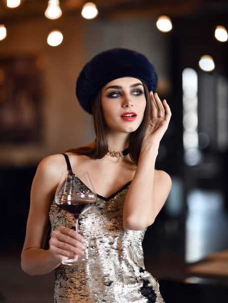 Beautiful woman wear dark blue winter mink fur hat drinking red wine in expensive restaurant  - Фото, зображення