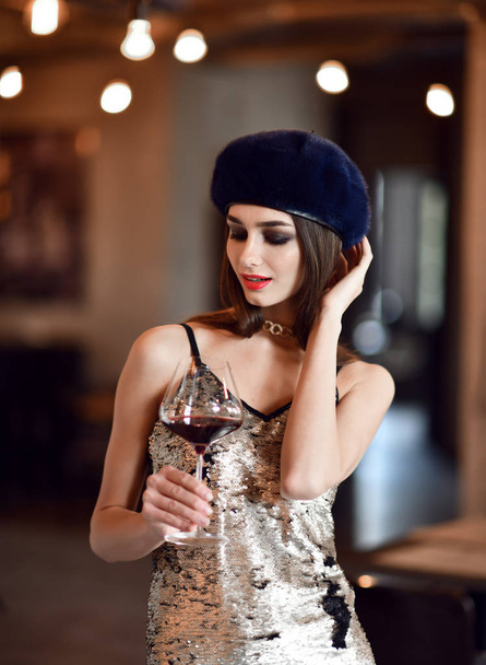 Beautiful woman wear dark blue winter mink fur hat drinking red wine in expensive restaurant  - Photo, Image