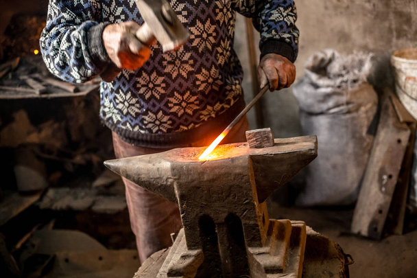 Vieux forgeron forgeant manuellement du métal fondu avec marteau sur l'enclume
. - Photo, image