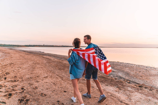 casal americano coberto de bandeira americana andando na praia
 - Foto, Imagem