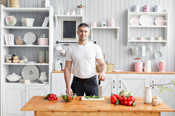 Retrato de un hombre guapo sonriente cortando verduras en la cocina. El concepto de productos ecológicos para cocinar
. - Foto, imagen