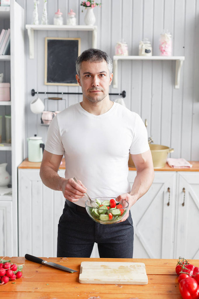 Портрет красивого улыбающегося мужчины, рубящего овощи на кухне. Концепция экологически чистых продуктов для приготовления пищи
. - Фото, изображение