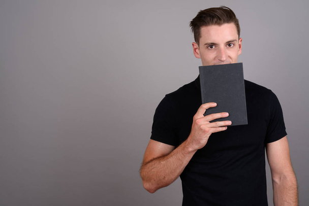 Young handsome student man hiding behind book - Φωτογραφία, εικόνα