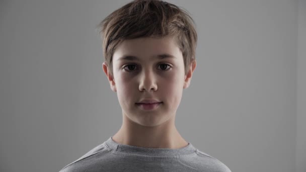 Πορτρέτο του χαριτωμένο νεαρή έτους 11-12 χρονών αγόρι κοιτάζοντας την κάμερα σε άσπρο φόντο - Πλάνα, βίντεο