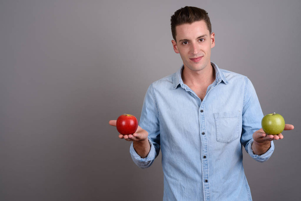 Όμορφος νεαρός που κατέχουν κόκκινο μήλο και πράσινο μήλο - Φωτογραφία, εικόνα