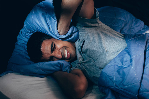 Mies peittää korvat tyynyllä sängyssä yöllä
 - Valokuva, kuva