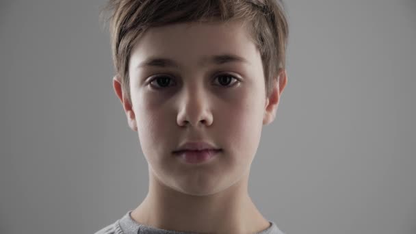 Portré, aranyos fiatal 11-12 év régi fiú nézi a kamerát a fehér háttér - Felvétel, videó