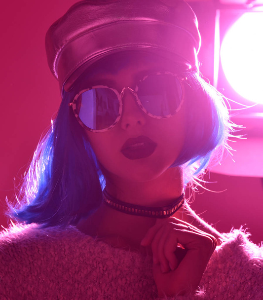 Woman in fashion winter concept wearing gold hat cap round sunglasses in pink neon light  - Фото, зображення