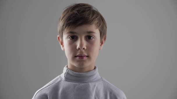 Portret cute młodych 11-12 roku chłopiec ogląda aparat na białym tle - Materiał filmowy, wideo