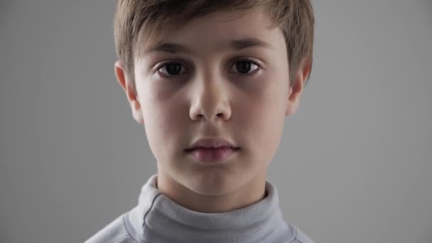 Közelről portré, aranyos fiatal 11-12 év régi fiú nézi a kamerát a fehér háttér - Felvétel, videó