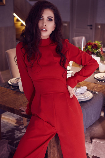 Porträt eines hinreißenden sinnlichen brünetten Modells im modischen roten Anzug, das im Wohnzimmer posiert. Innenaufnahme. - Foto, Bild