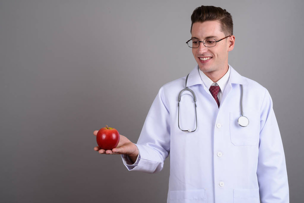 Молодий щасливий лікар тримає червоне яблуко, посміхаючись
 - Фото, зображення