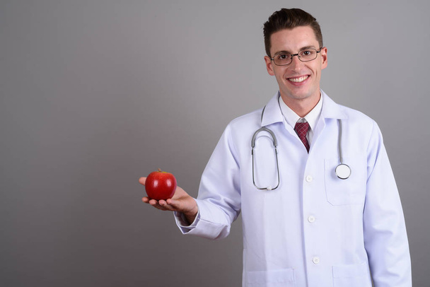 Молодой счастливый человек доктор держит красное яблоко, улыбаясь
 - Фото, изображение
