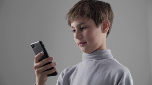 Retrato de niño pequeño usando Smartphone sobre fondo blanco. Chico trenzado juegos en el teléfono inteligente
. - Metraje, vídeo