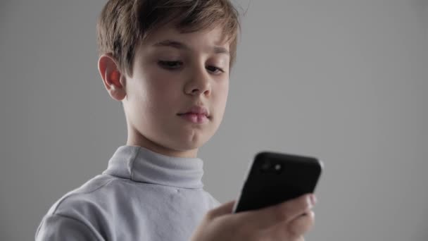 Retrato de niño pequeño usando Smartphone sobre fondo blanco. Chico trenzado juegos en el teléfono inteligente
. - Imágenes, Vídeo