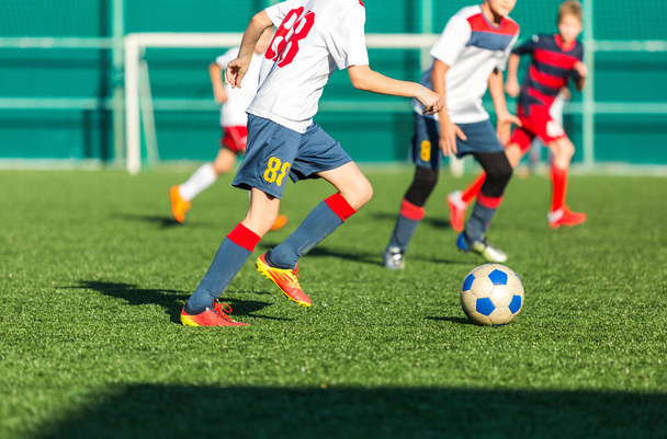 football teams - boys in red, blue, white sportswear play soccer on the green field. boys dribbling. dribbling skills. Team game, training, active lifestyle, hobby, sport for kids concept - Photo, Image