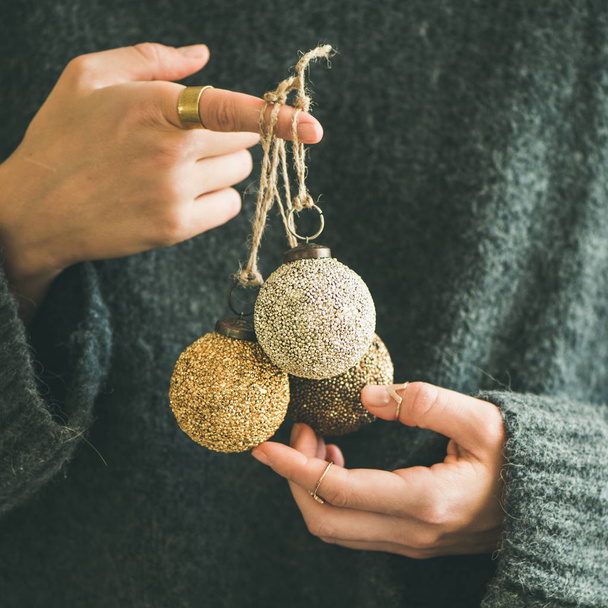 Woman in grey warm woolen sweater holding toy golden decorative balls in hands, copy space, square crop. Christmas, new year holiday celebration concept - Foto, afbeelding