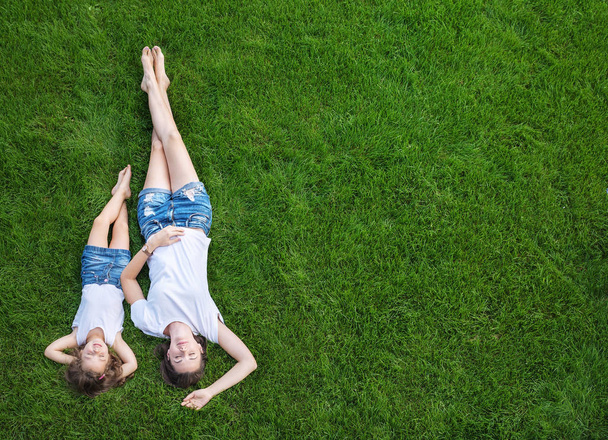 Conceptual portrait of a pretty mother relaxing with daughter on a fresh, green lawn - 写真・画像