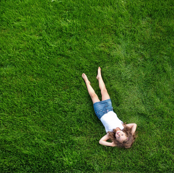 Niña relajada acostada en un prado verde y fresco
 - Foto, imagen
