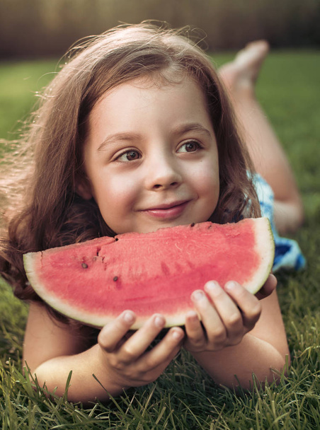 Closeup portrait of smiling child holding watermelon slice in the garden - Photo, Image