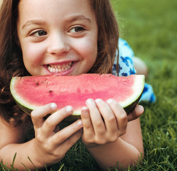 Closeup portrait of smiling child holding watermelon slice in the garden - Photo, Image