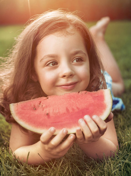 Портрет улыбающегося ребенка с ломтиком арбуза в саду
 - Фото, изображение