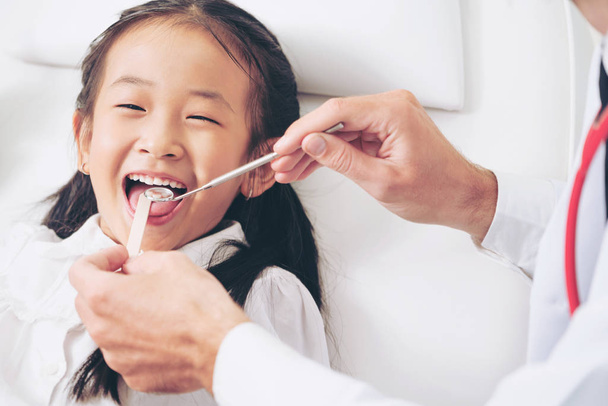 Дружній молодий стоматолог вивчає щасливі дитячі зуби в стоматологічній клініці. Концепція стоматології
. - Фото, зображення