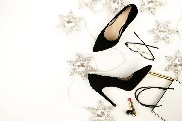 Women's black high heels shoes and accessories glasses, cosmetics, lipstick, bag, Christmas garland top view on a white background.  Holiday fashion concept. Flat lay.  - Foto, imagen
